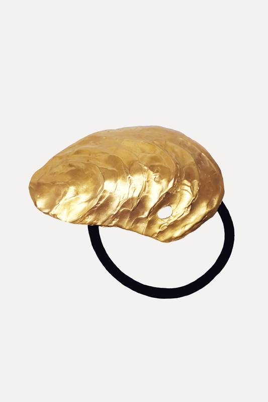 A bronze hair tie with an oyster shell shape, finished with an 18k gold plating, displayed on a white background.